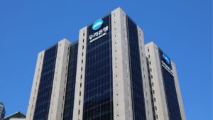 Modern high-rise bank building featuring Woori Bank logos on a blue glass facade against a clear blue sky.