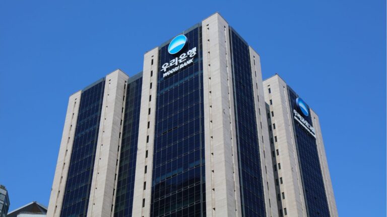 Modern high-rise bank building featuring Woori Bank logos on a blue glass facade against a clear blue sky.