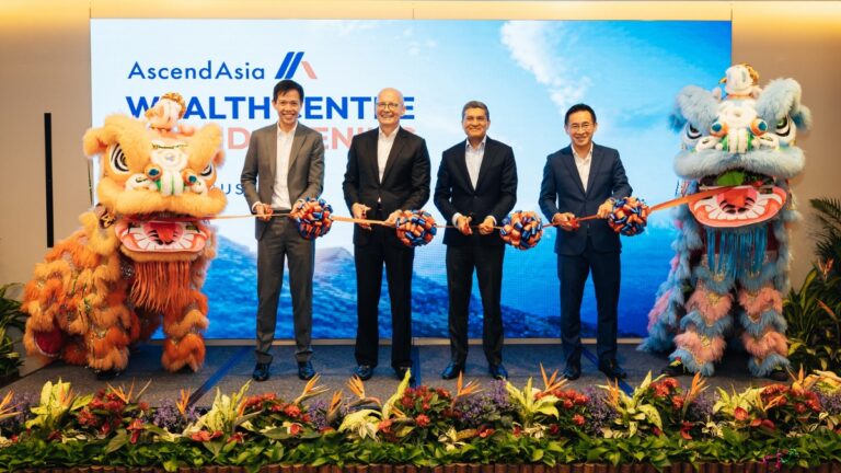 Five executives in suits cut a ceremonial ribbon at a launch event, flanked by orange and blue lion dancers on stage with a blue backdrop.
