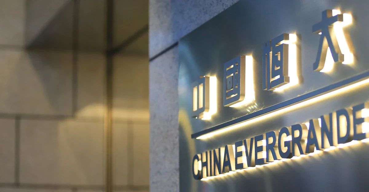 Illuminated China Evergrande sign on a dark metal plaque, with Chinese characters above the company name in a lobby setting.
