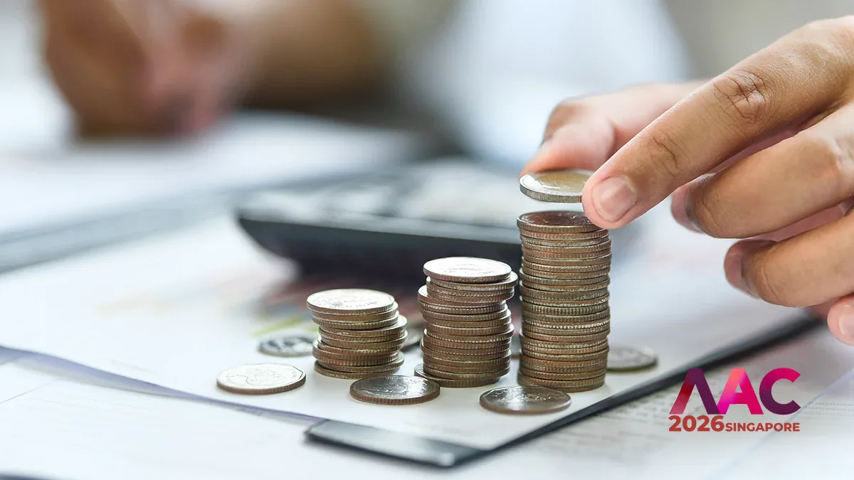 Hands stacking coins on a financial document with a calculator in the background; logo reads AC 2026 Singapore on the corner by the coins.