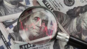 Magnifying glass over US dollar bills with red stock chart lines, suggesting financial analysis or scrutiny.