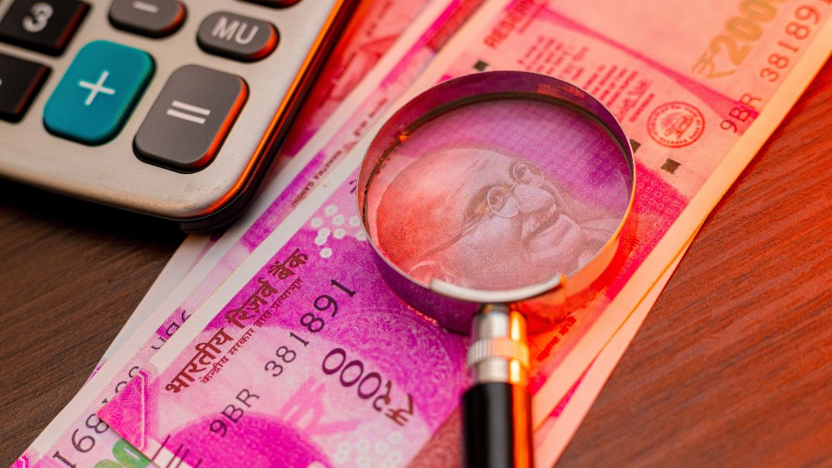 Magnifying glass over colorful Indian banknotes beside a calculator, suggesting financial scrutiny or budgeting.