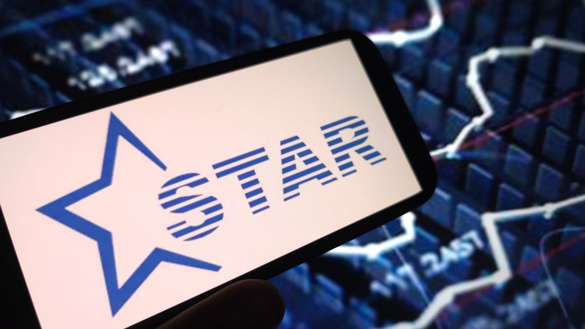 Tablet screen displaying the GSTAR logo with a blue star, held against a background of stock market charts.