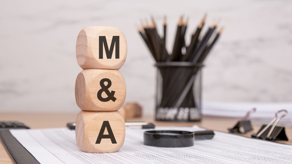 Wooden blocks showing M & A on a desk, symbolizing mergers and acquisitions with office supplies in the background.