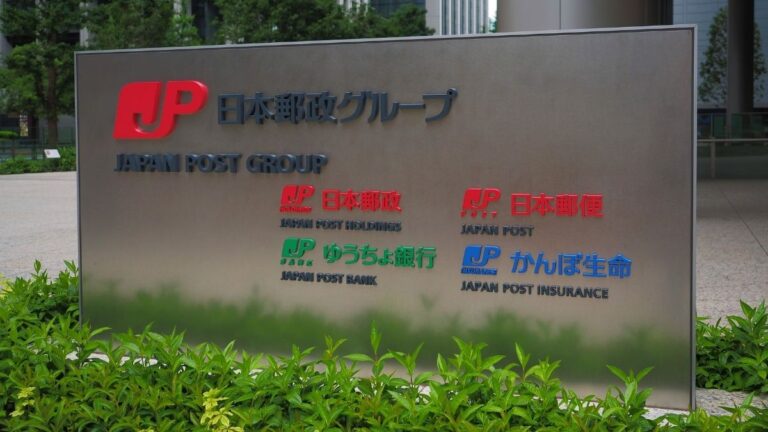 Metal signboard outside a building showing Japan Post Group and logos for Japan Post Holdings, Bank, Insurance, and related services with English and Japanese text.