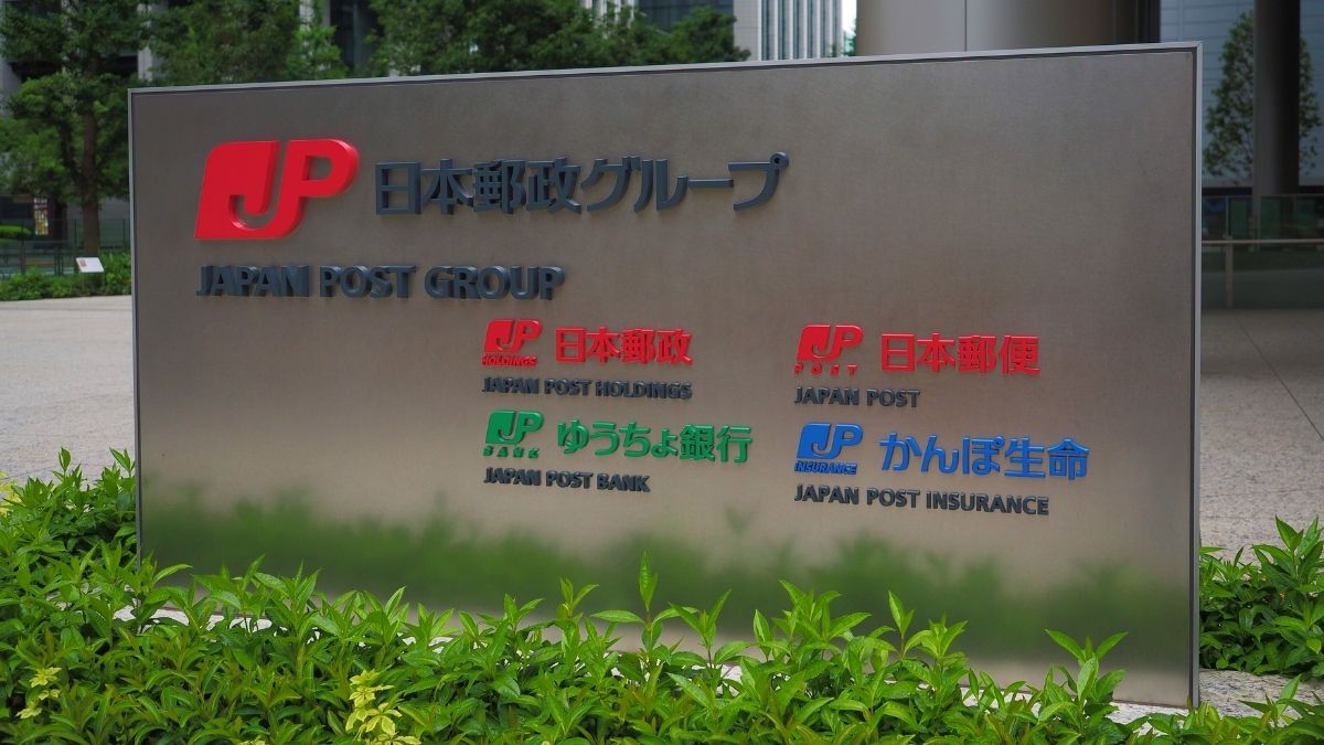 Metal signboard outside a building showing Japan Post Group and logos for Japan Post Holdings, Bank, Insurance, and related services with English and Japanese text.
