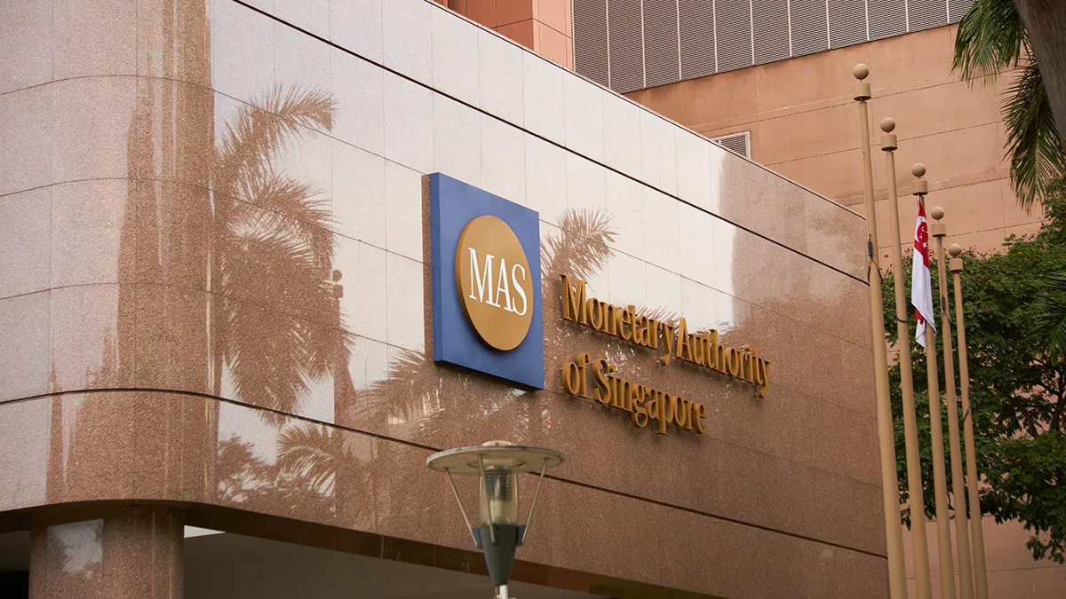 MAS sign on a tan granite building with palm tree reflections and flagpoles.
