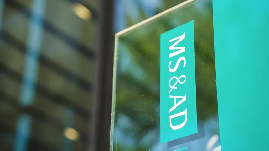 Close-up of a teal glass door sign reading 'MS & AD' with blurred building reflections in the background