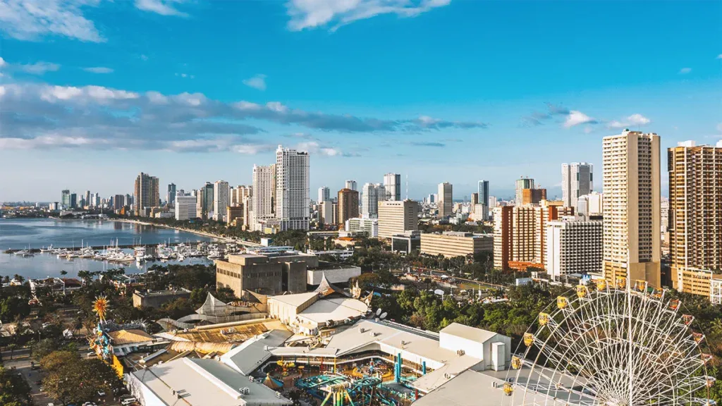 Aerial view of a coastal city skyline with high-rise buildings, a marina, and a large Ferris wheel in the foreground.