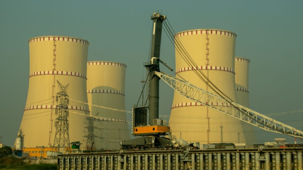 Industrial power plant with large cooling towers and a crane in the foreground, high-voltage lines nearby