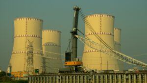 Industrial power plant with large cooling towers and a crane in the foreground, high-voltage lines nearby