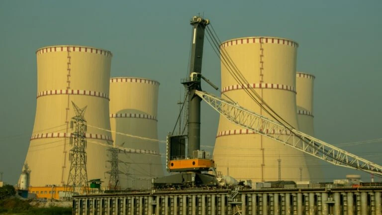 Industrial power plant with large cooling towers and a crane in the foreground, high-voltage lines nearby
