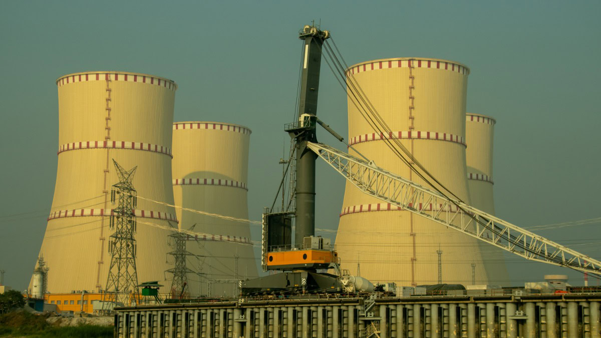 Industrial power plant with large cooling towers and a crane in the foreground, high-voltage lines nearby