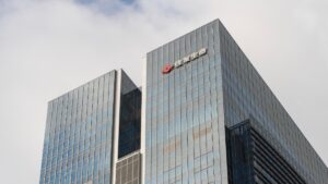 Glass office skyscraper with a red company logo and Chinese text at the top corner, reflecting in the facade.