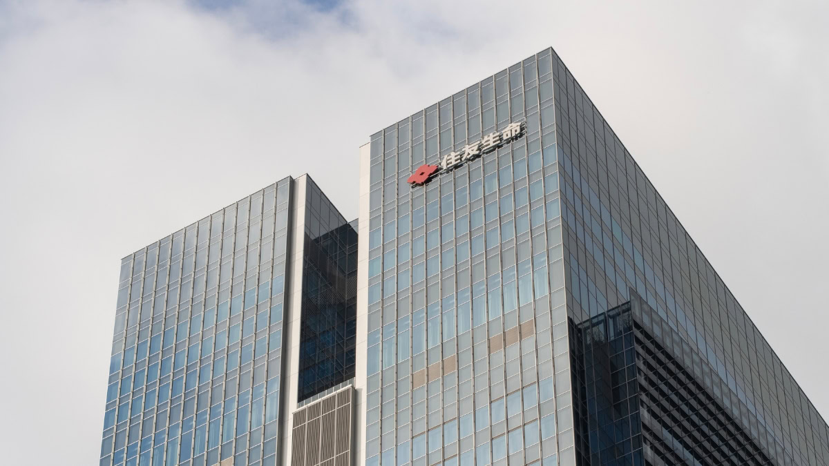 Glass office skyscraper with a red company logo and Chinese text at the top corner, reflecting in the facade.
