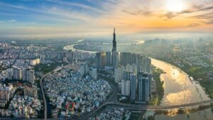 Aerial view of a densely built city with a winding river, high-rise towers, and a sunset sky above the skyline.
