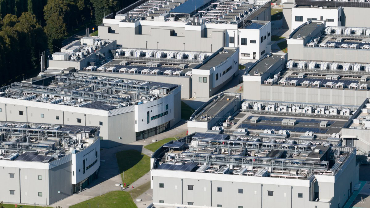 Industrial complex with multiple white buildings and rooftop equipment.