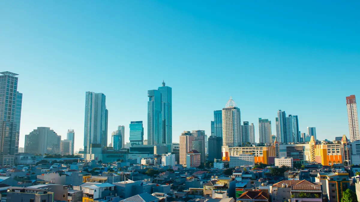 Modern city skyline with high-rise towers above a dense neighborhood under a clear blue sky.