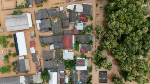 APAC property insurers to rely on repricing, reinsurance as climate risks grow: Moody's Aerial view of muddy floodwaters surrounding homes, roads and trees in a densely built settlement.