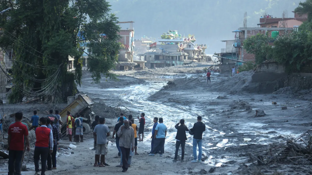 People gather to survey mud and debris covering a residential street.
