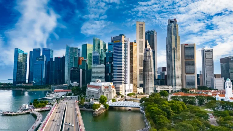 Singapore skyline with high-rise office towers, Marina Bay waters and a bridge under a partly cloudy sky.