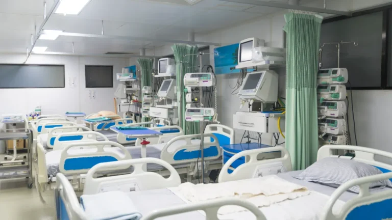 Hospital ward with multiple beds, monitors, infusion pumps and privacy curtains.