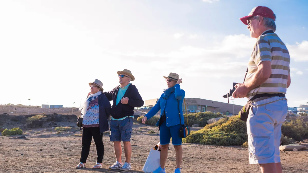 Four older adults walk along a sunny coastal trail.
