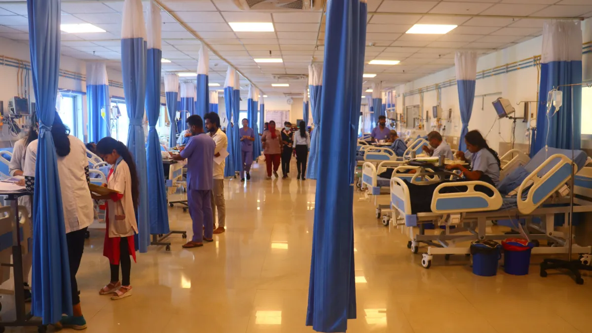 Hospital ward with blue privacy curtains, patients in beds, and medical staff attending to them.