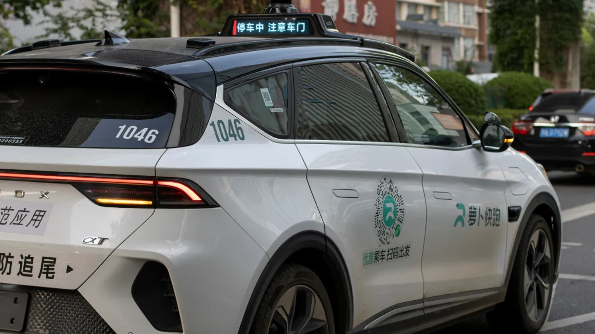A white autonomous-driving taxi marked with Chinese text travels along a city street.