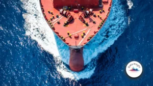 Aerial view of a cargo ship cutting through deep blue ocean water.