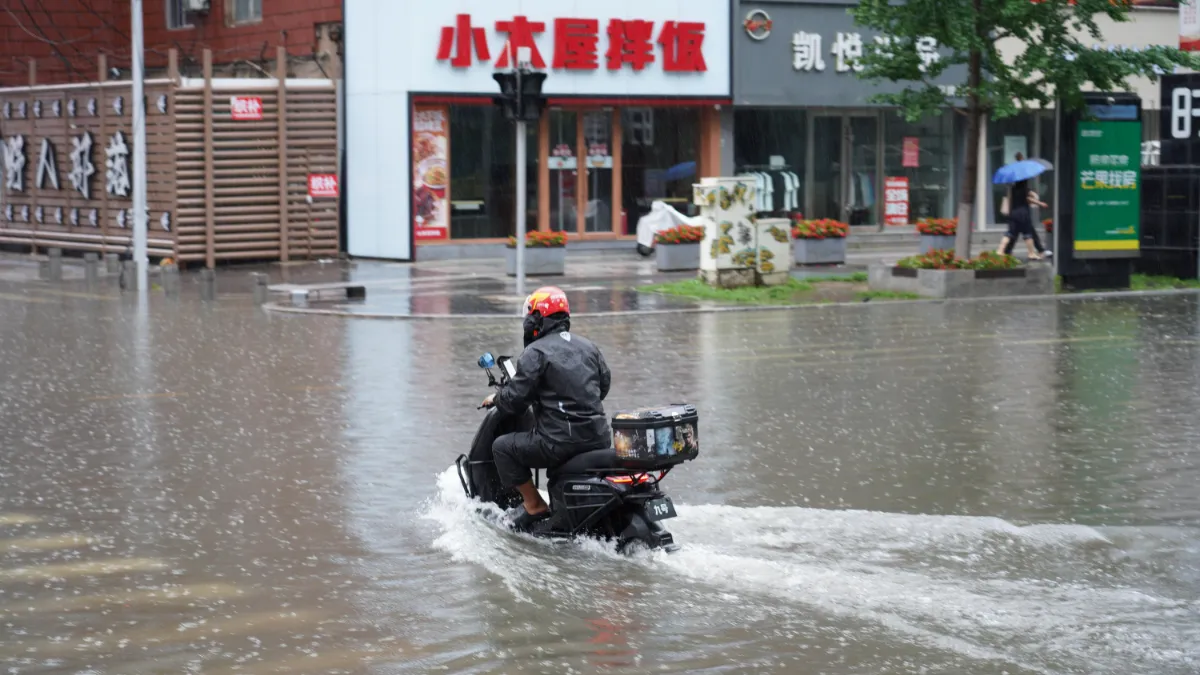 A scooter rider navigates a flooded street in heavy rain in China.