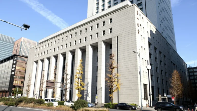 Exterior of a large stone office building with tall columns and a tower against a blue sky.
