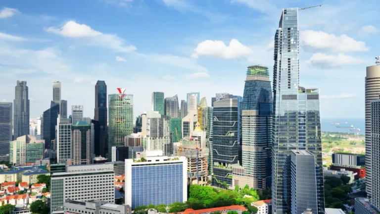 Dense city skyline with modern high-rises, a waterfront, and blue sky.