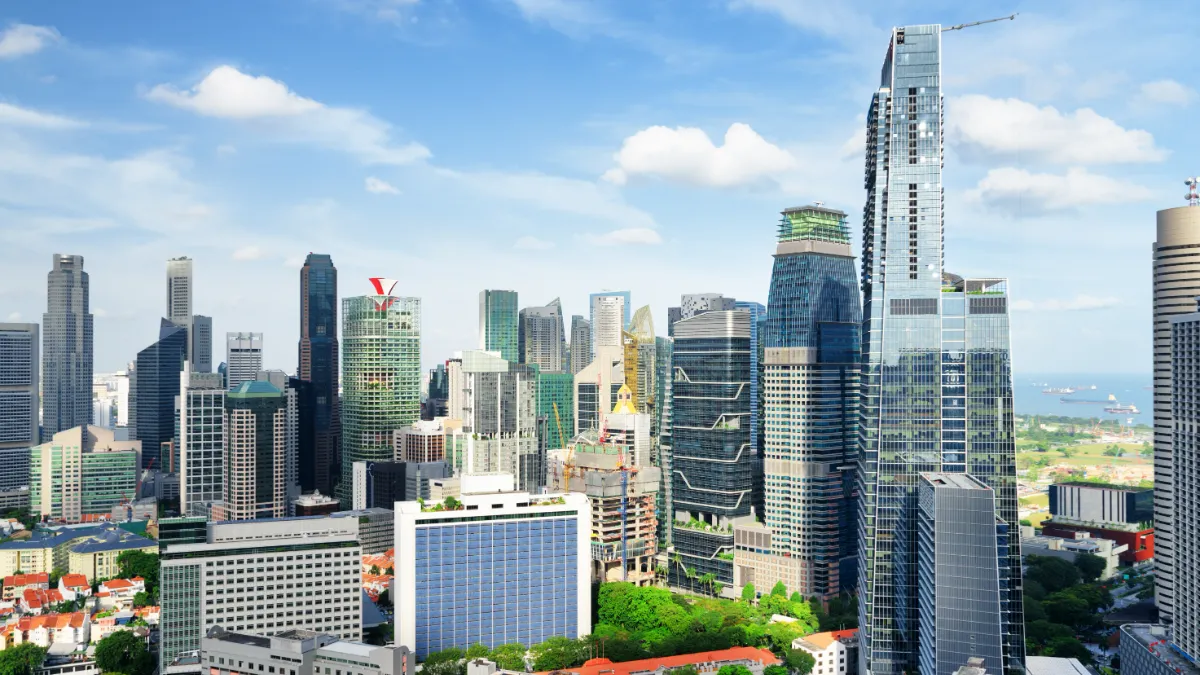 Dense city skyline with modern high-rises, a waterfront, and blue sky.