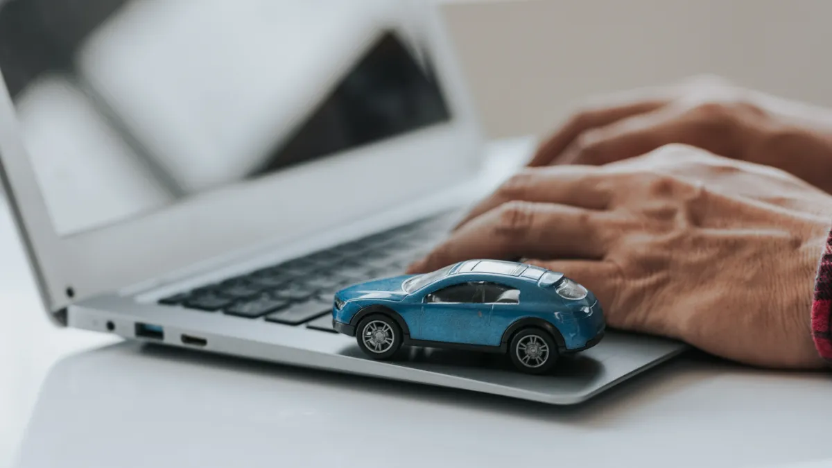 Hands type on a laptop beside a blue toy car.