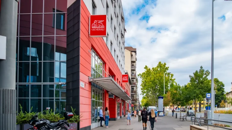 Generali building with red signs on a city street, with pedestrians walking outside.