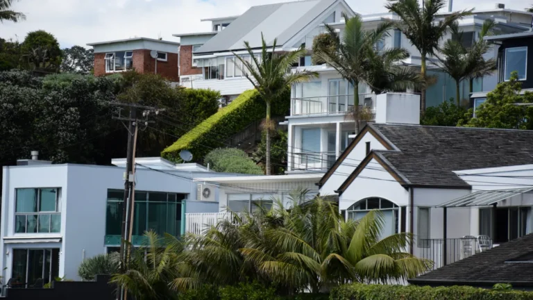Modern homes with balconies, palm trees and lush greenery on a densely built hillside.