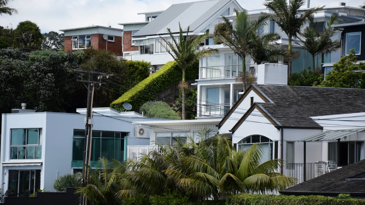 Modern homes with balconies, palm trees and lush greenery on a densely built hillside.