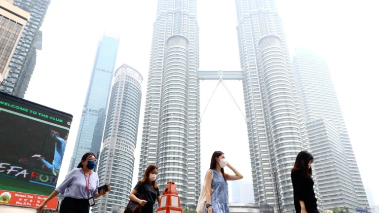 Masked pedestrians walk in front of Kuala Lumpur’s Petronas Twin Towers.