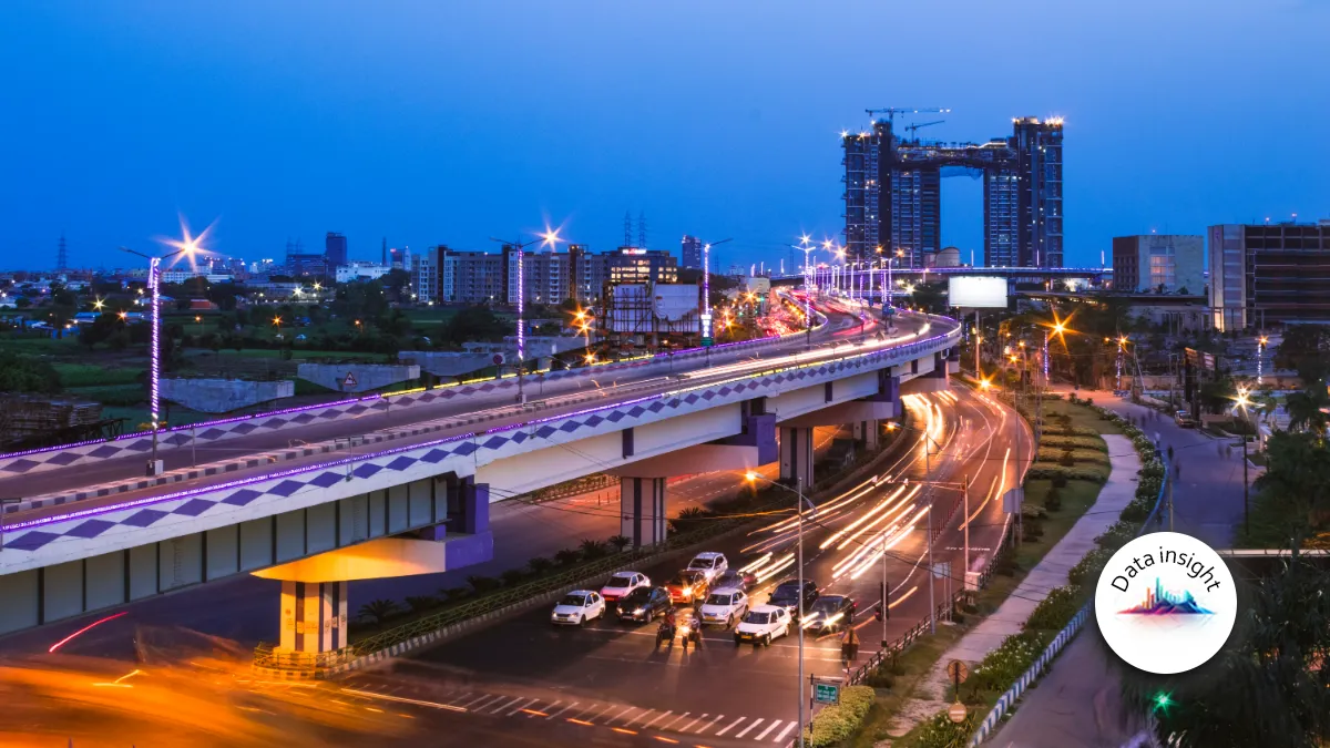 Nighttime cityscape with an illuminated elevated highway, traffic light trails and modern high-rise buildings.