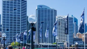 IAG, RAC challenge ACCC’s A$1.35bn deal block at tribunal Sydney skyline with IAG and Rabobank office towers, surrounded by branded flags and streetlamps.