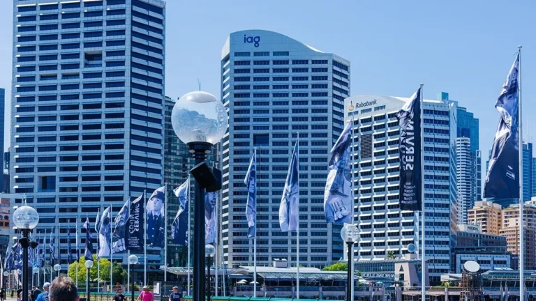 Sydney skyline with IAG and Rabobank office towers, surrounded by branded flags and streetlamps.