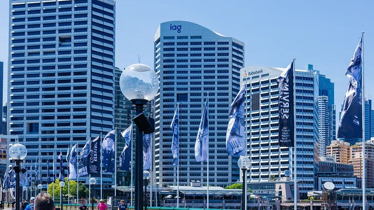Sydney skyline with IAG and Rabobank office towers, surrounded by branded flags and streetlamps.