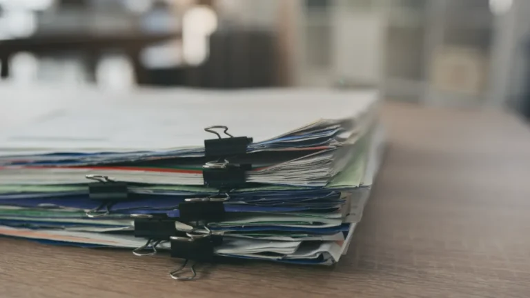 Stack of documents secured with black binder clips on a wooden desk.