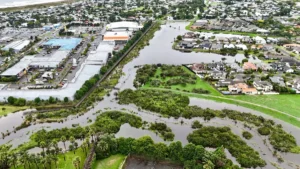 ICNZ calls for long-term government funding to safeguard insurance affordability Aerial view of floodwaters surrounding homes, shops, railway tracks and green space.