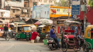 India's GIC weighs proposal for 10% mandatory co-payment on retail health policies — report Busy Indian street with auto-rickshaws, a cycle rickshaw, scooters, pedestrians and market signs.