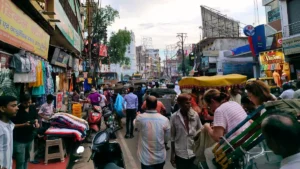 IRDAI chairman calls for rethink of insurance effectiveness metrics A crowded Indian market street with shoppers, clothing stalls, auto-rickshaws and a cycle rickshaw.