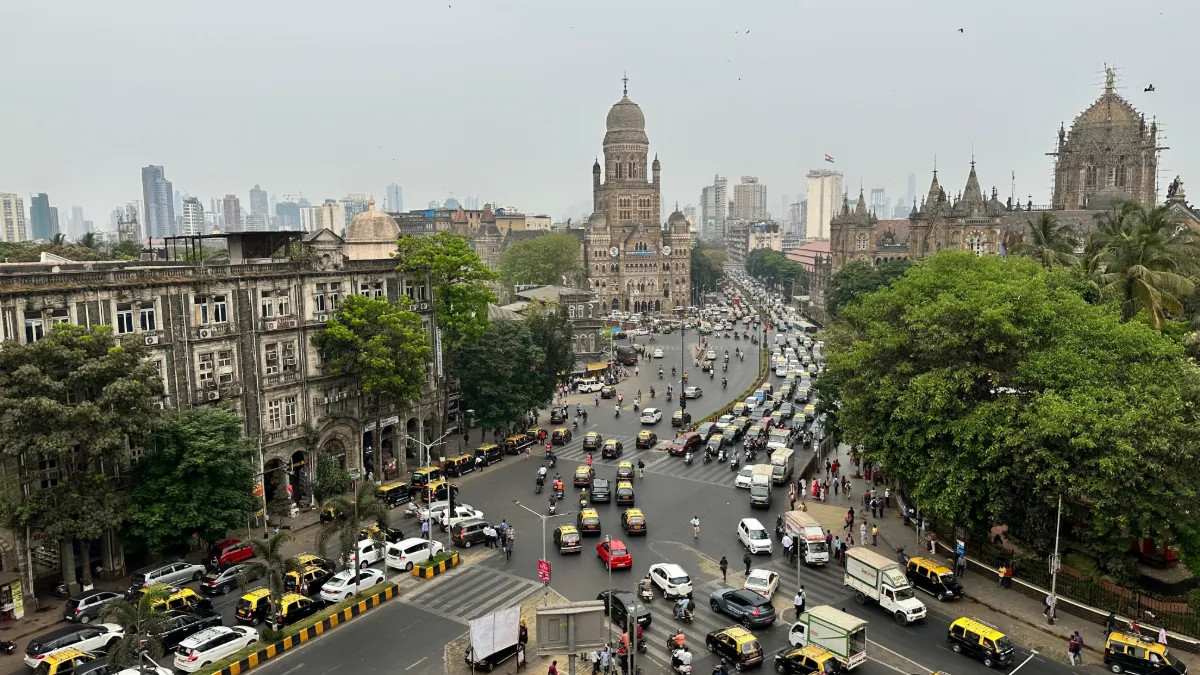 Busy Mumbai intersection with historic Gothic buildings, dense traffic, trees and high-rises in the background.