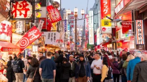 Japan weighs captive framework to expand corporate risk-financing options Crowded Osaka shopping street lined with colorful Japanese signs, lanterns, restaurants and pedestrians.